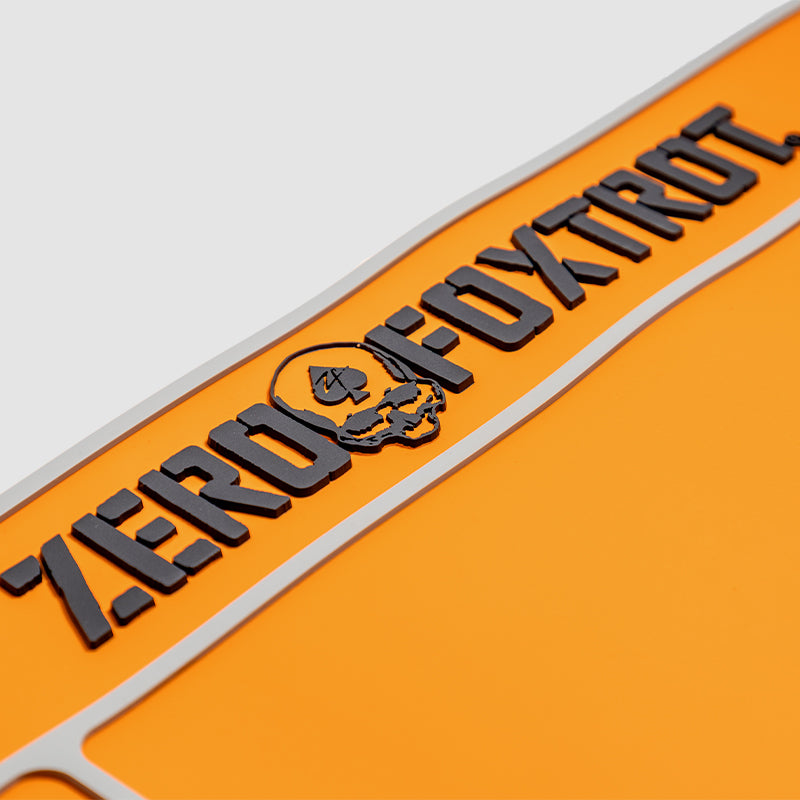 Close-up of the orange ZF Gun Cleaning Mat featuring raised black lettering and a skull logo on a textured surface designed for firearm maintenance.