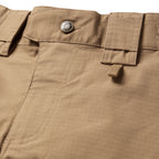 Tac Pants in tan fabric with a buttoned waistband, belt loops, flap pockets, reinforced grid stitching, and detailed seam construction closeup