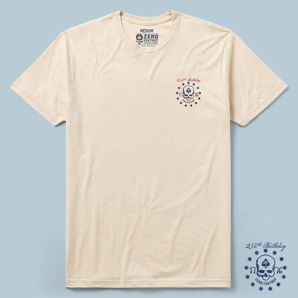 Oathbound Tee in a light beige color featuring a small navy and red skull and star design on the left chest with the text "2.1.76 Birthday" and "Zero Foxtrot" printed above and below the graphic.