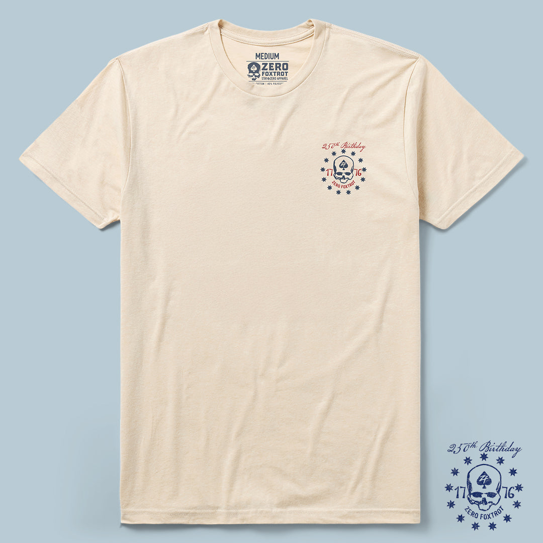 Oathbound Tee in a light beige color featuring a small navy and red skull and star design on the left chest with the text "2.1.76 Birthday" and "Zero Foxtrot" printed above and below the graphic.