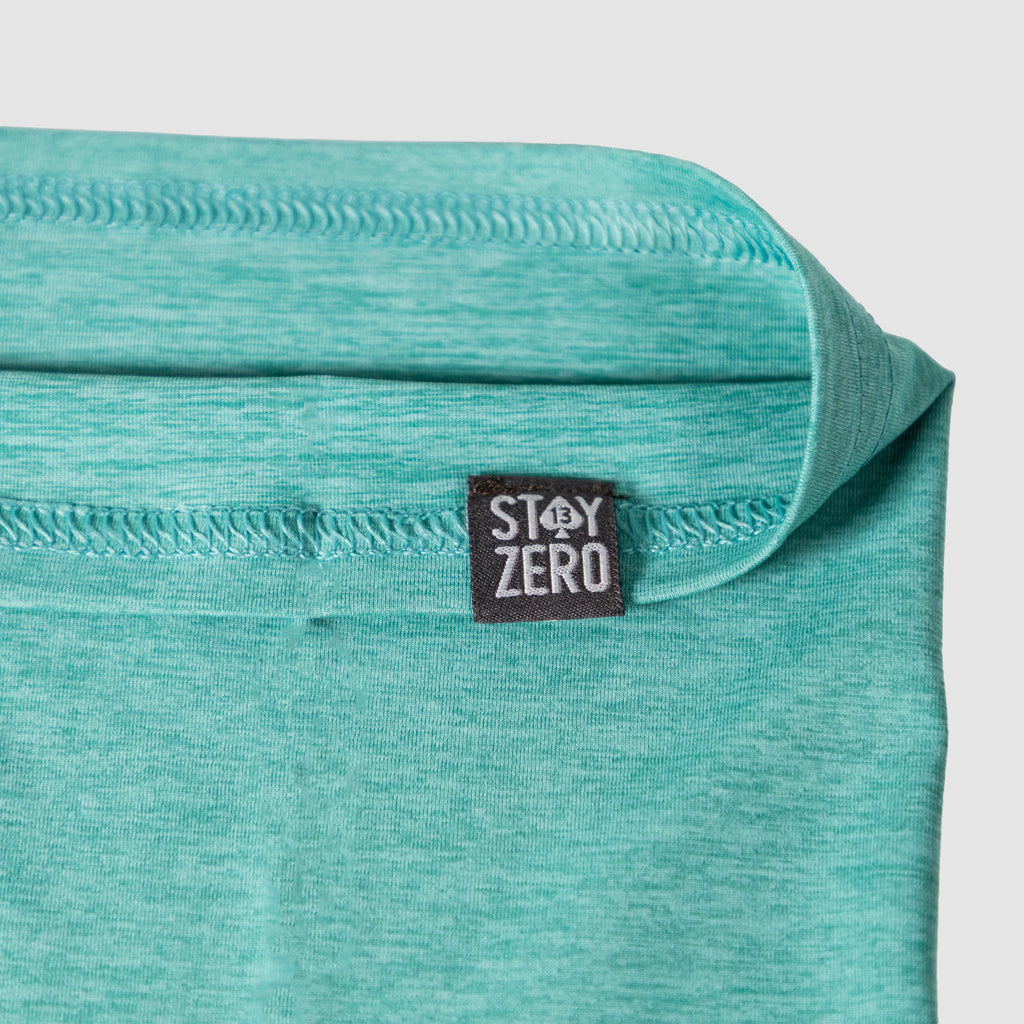Close-up view of a turquoise fabric Performance Sun Gaiter with a visible black tag labeled Stay Zero, highlighting the material texture and stitching details.
