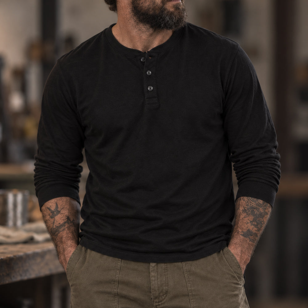Long Sleeve Cotton Skivvy Henley in black with a button placket, modeled with sleeves pushed up and hands in pockets.