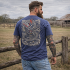 Man with tattoos wearing a blue Focused Fury Tee featuring an intricate dragon and samurai sword design on the back, standing outdoors by a wooden fence in a rural setting.