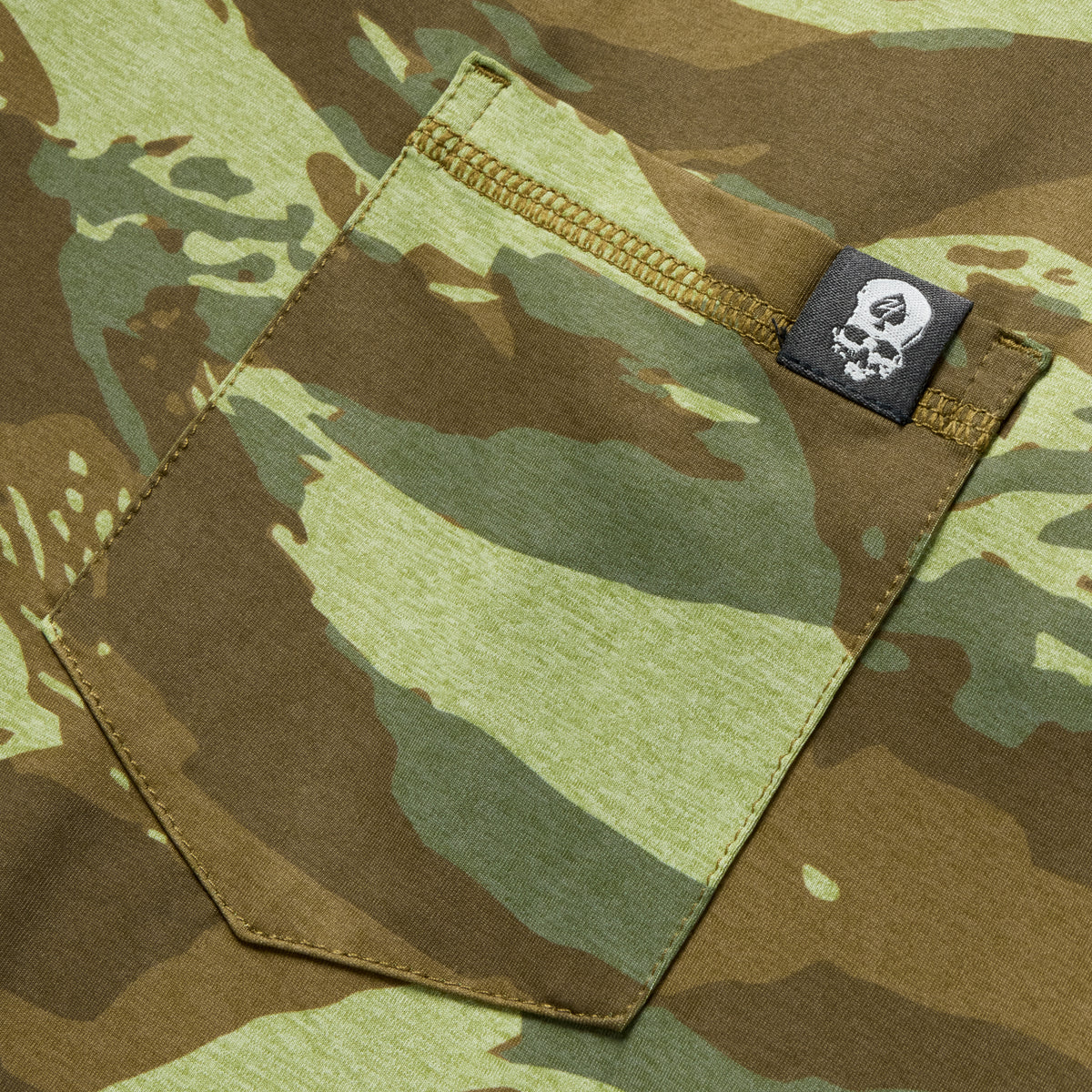 Close-up of a woodland-style camo pocket with reinforced stitching and branded tag on a Performance Sun Hoodie in muted green and brown tones.