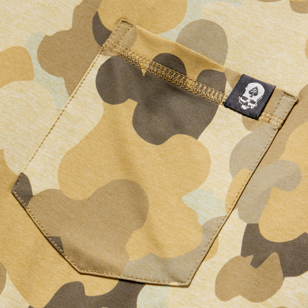 Close-up of a tan and brown camo patterned pocket with a small black tag featuring a white logo on a Performance Sun Hoodie.