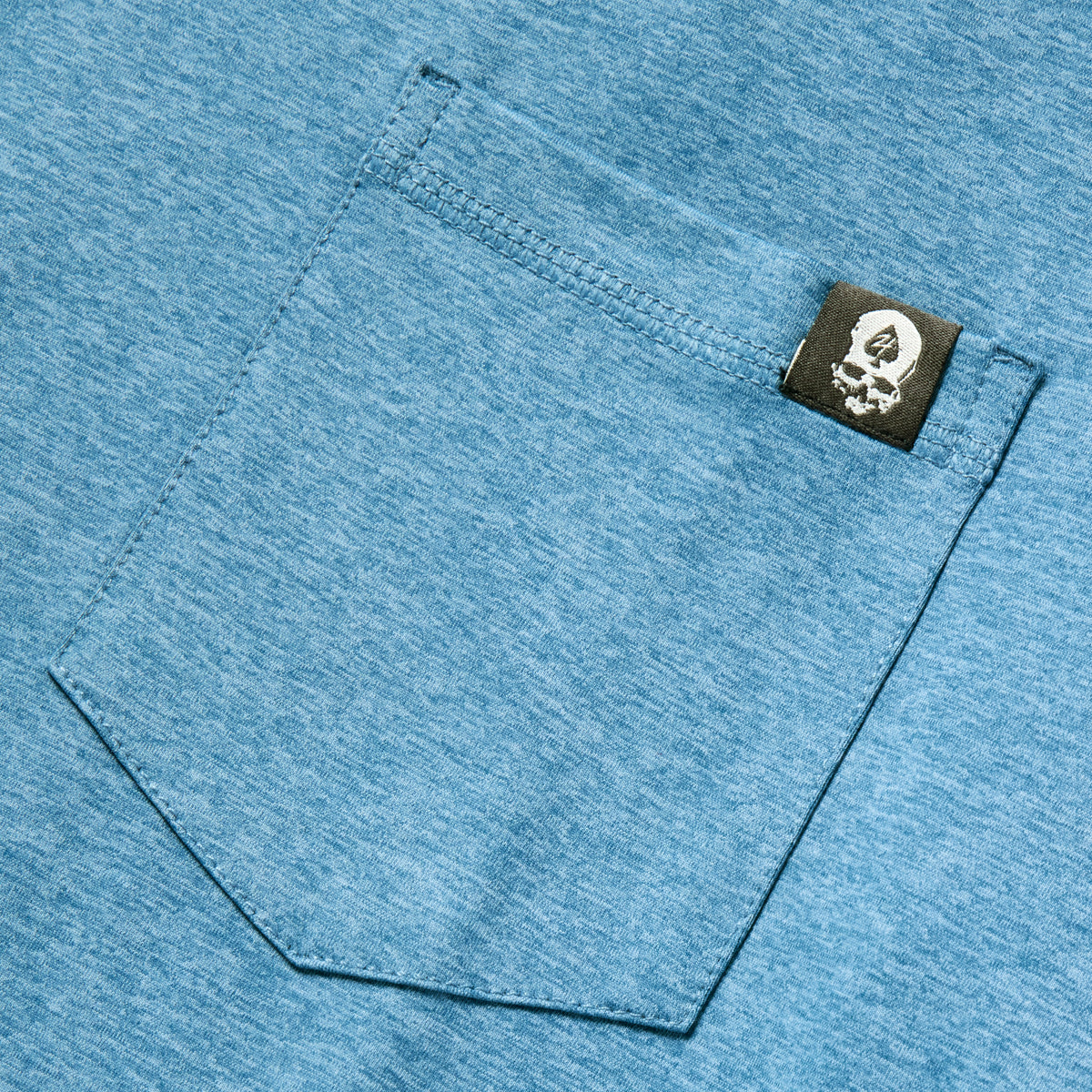Close-up of an ocean blue Performance Sun Hoodie showing a textured fabric pocket with a small black tag featuring a white logo, highlighting the material and stitching detail.