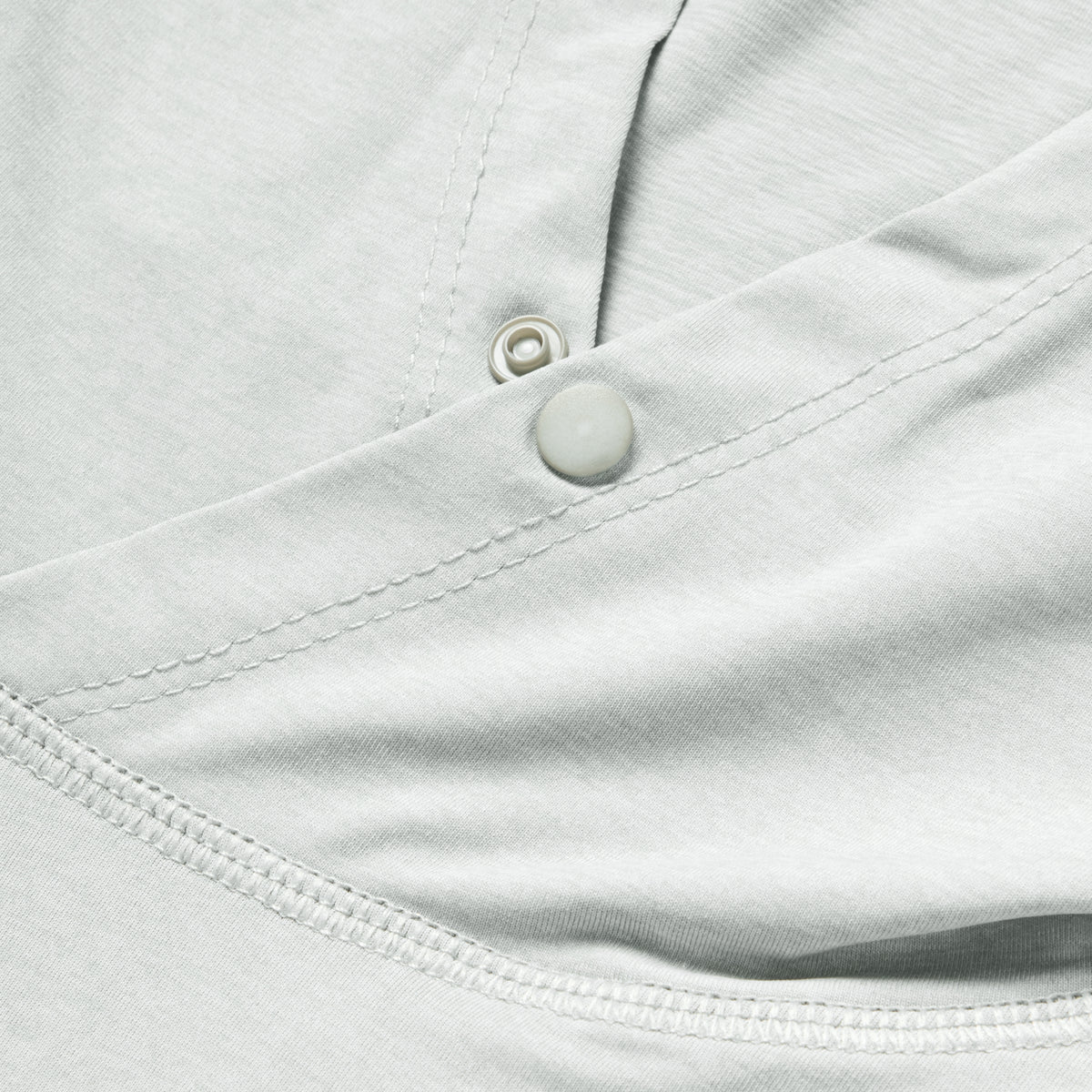 Close-up detail of light gray fabric with stitching and snap button of the Performance Sun Hoodie, highlighting its smooth texture and durable construction.