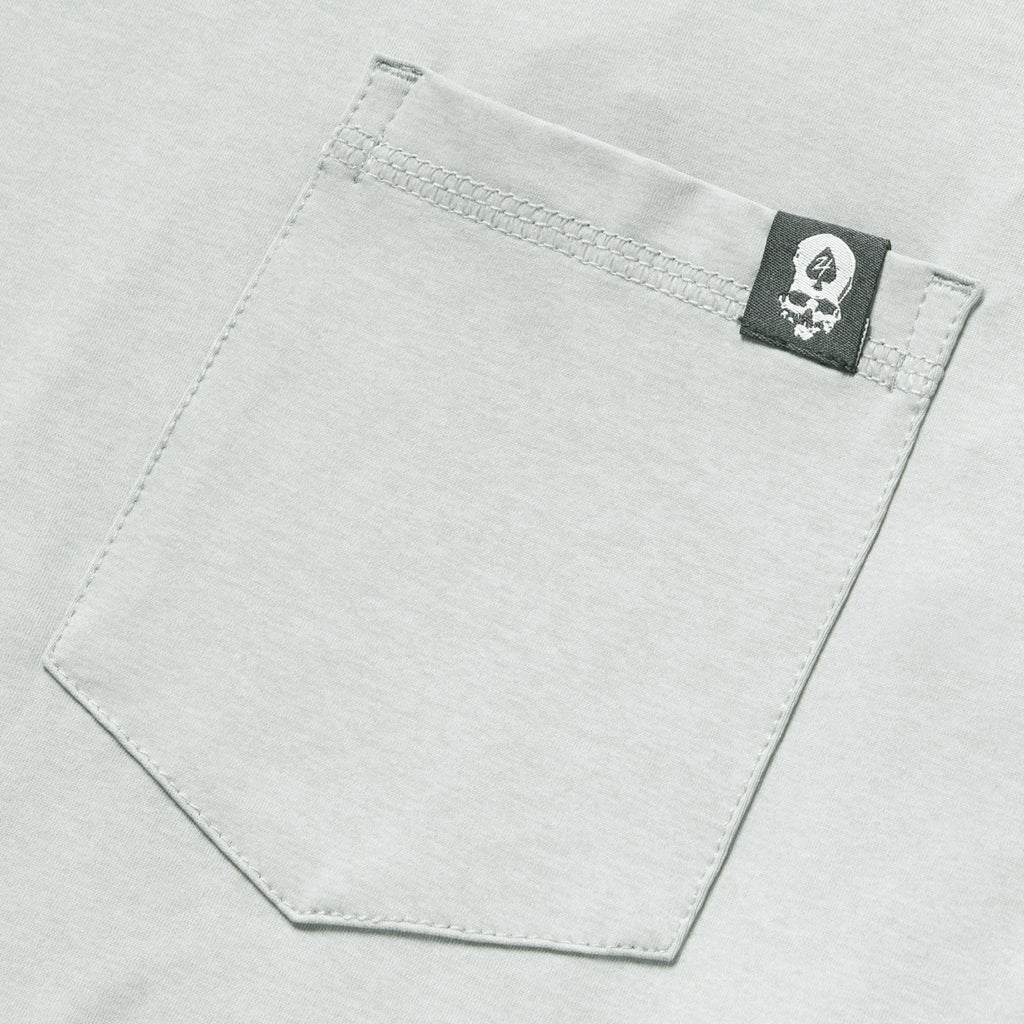 Close-up of a light gray fabric pocket with a small black and white skull logo tag on a Performance Sun Hoodie.