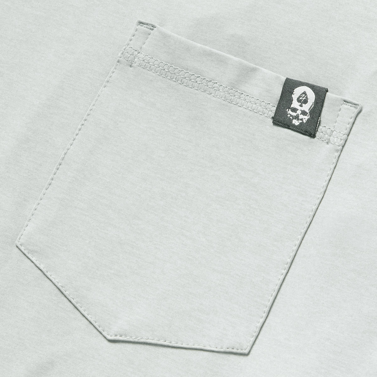 Close-up of a light gray fabric pocket with a small black and white skull logo tag on a Performance Sun Hoodie.
