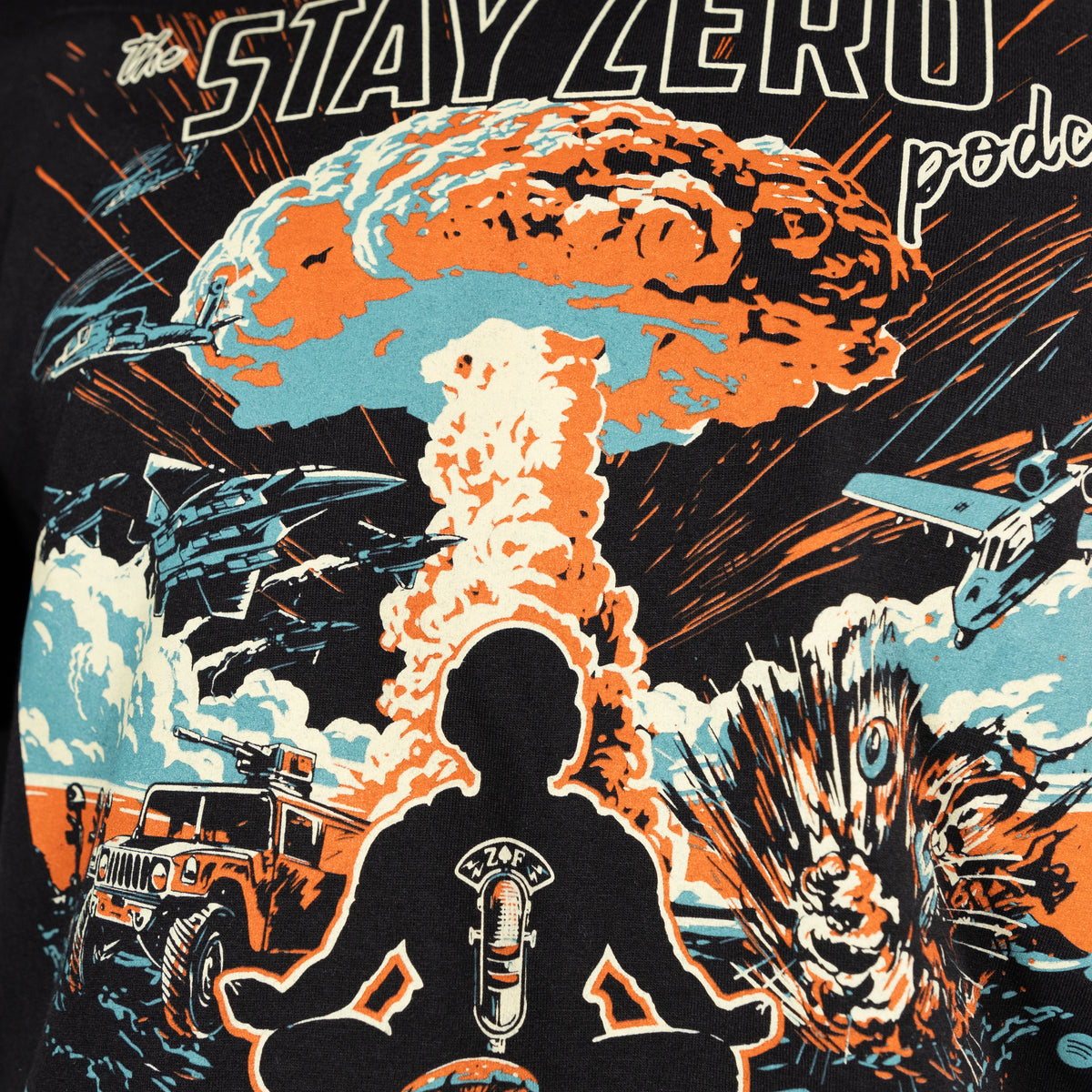Close-up of a graphic on the Podcast Boom Tee showing a silhouette of a person meditating with a microphone symbol, surrounded by explosions, military vehicles, and aircraft against a dramatic, fiery background.