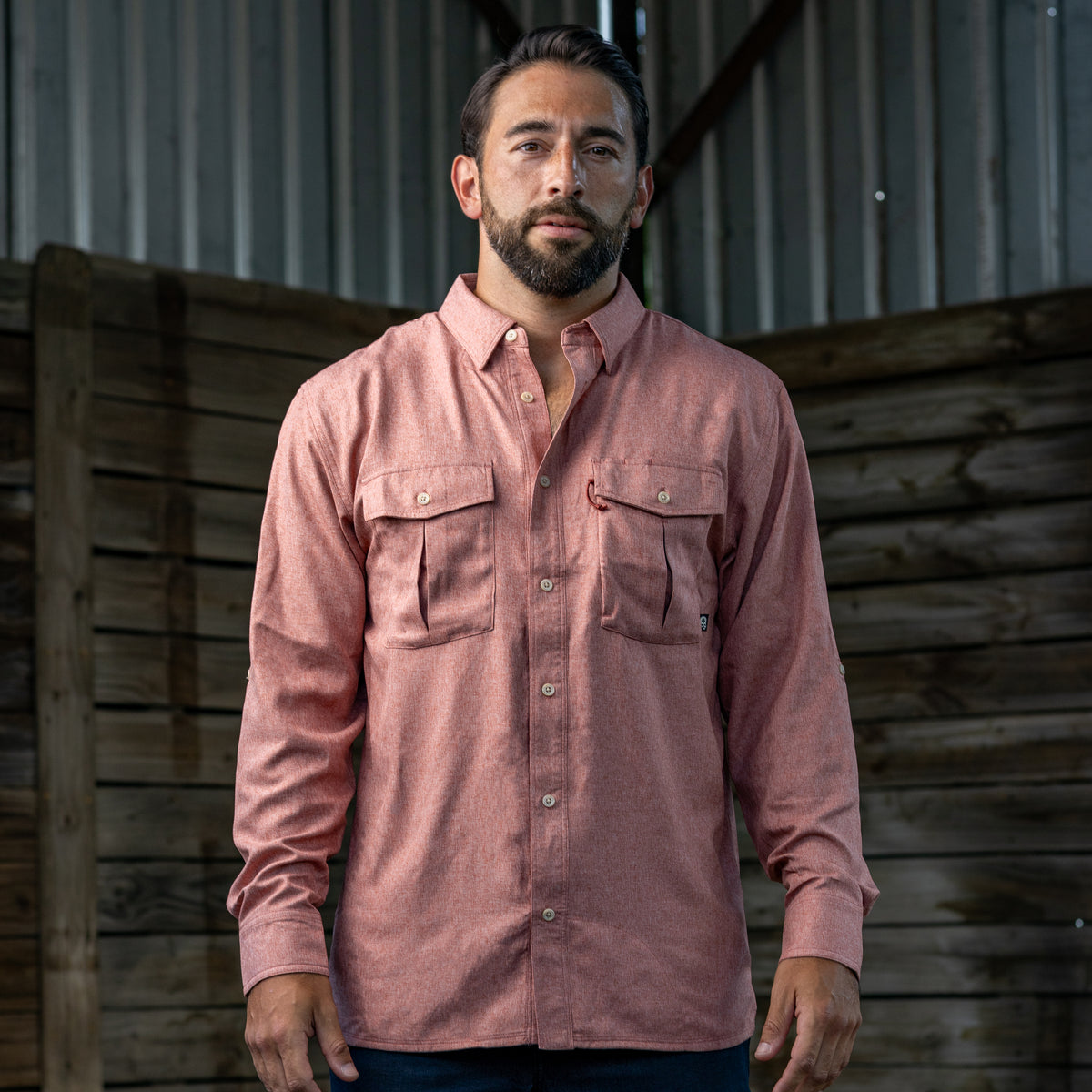 Man wearing a long-sleeve, button-up pink shirt with two chest pockets in a rustic wooden setting, showcasing the F'n Soft Daily Shirt.
