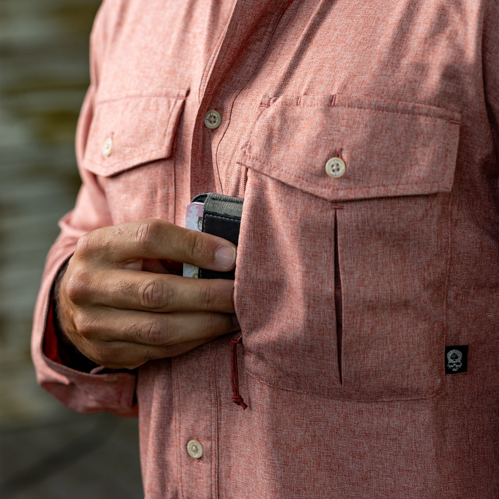 Close-up of a person wearing a textured red F'n Soft Daily Shirt, placing a wallet into the left chest pocket with button flap detail and a small black logo tag.