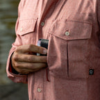 Close-up of a person wearing a textured red F'n Soft Daily Shirt, placing a wallet into the left chest pocket with button flap detail and a small black logo tag.