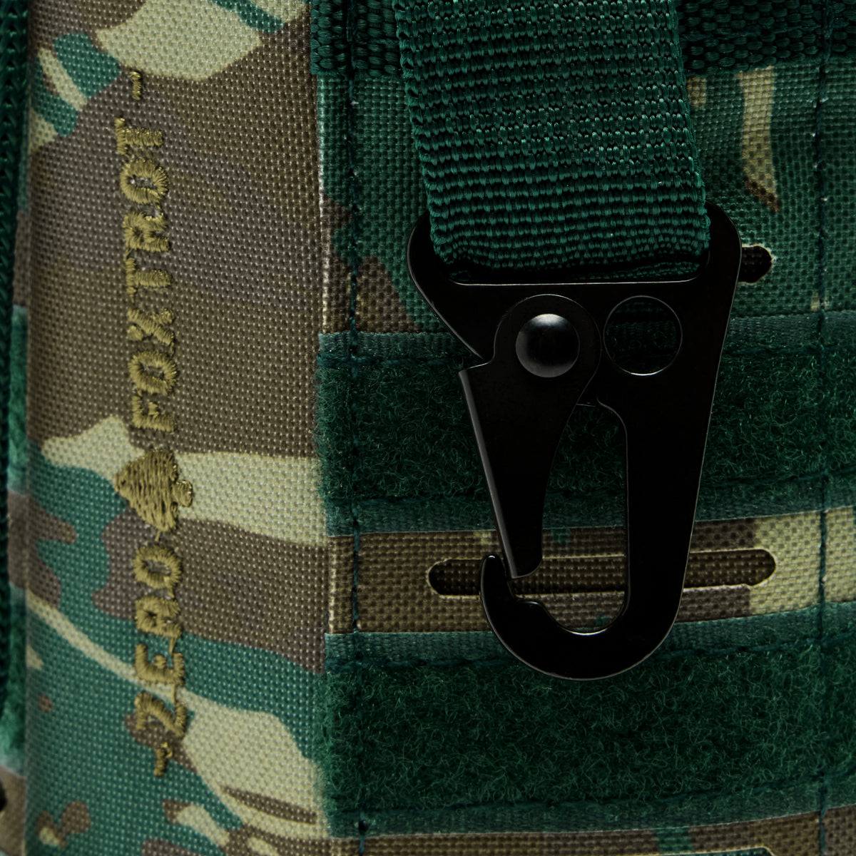 TAC Ruck Bottle - 64oz close up showing a black carabiner clip attached to green webbing on a camouflage carrier panel