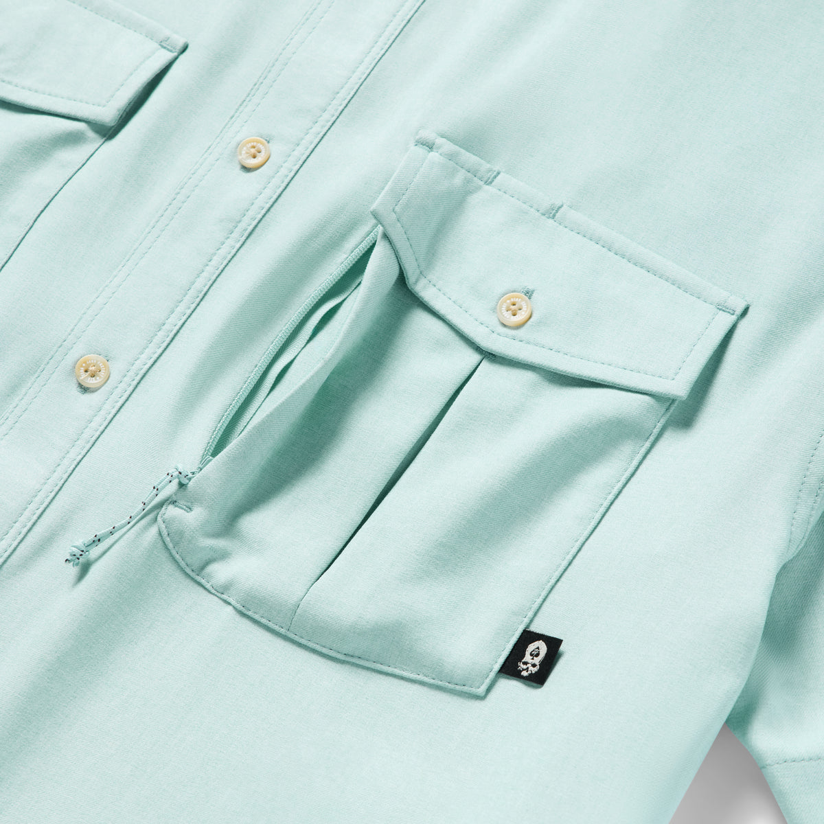 Close-up of a light aqua fabric pocket with a flap and button detail on the Short Sleeve F'n Soft Shirt, highlighting its soft texture and functional design.
