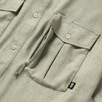 Close-up of a sage green Short Sleeve F'n Soft Shirt showing a buttoned flap pocket with a zipper underneath and a small black tag with a skull logo.