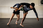 Compression Long Sleeve Rash Guard worn by a grappler practicing takedown drills with a partner on a padded training mat