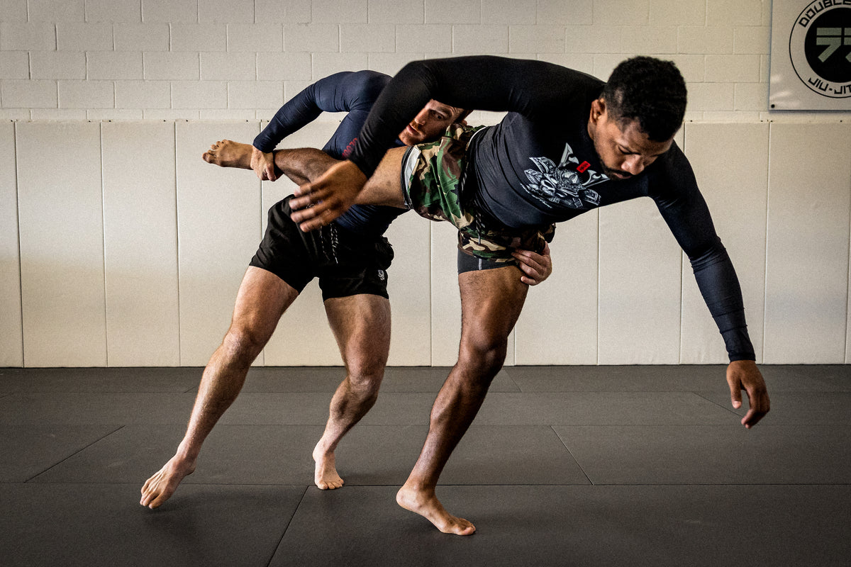 Compression Long Sleeve Rash Guard worn by a grappler practicing takedown drills with a partner on a padded training mat