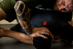Compression Long Sleeve Rash Guard worn during a grappling training session, with a black athletic top visible as two athletes practice on the mat