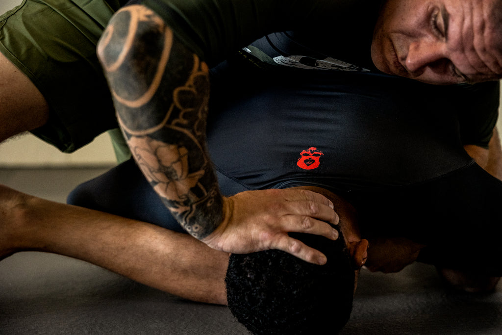 Compression Short Sleeve Rash Guard worn by a man during training, shown in black with a small red chest logo and short sleeves.