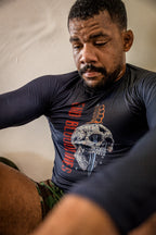 Compression Long Sleeve Rash Guard worn by a man, featuring a fitted black design with a skull graphic and red and orange lettering while he exercises.