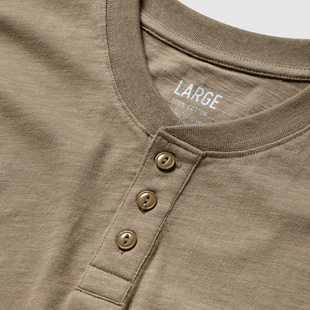 Close-up of a large short sleeve cotton skivvy henley in a muted brown shade, featuring a round neckline and three matching buttons on the placket.