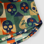 Close-up of fabric featuring a colorful geometric skull pattern in blue, green, orange, and beige tones, part of the Geo Skulls Silkies garment.