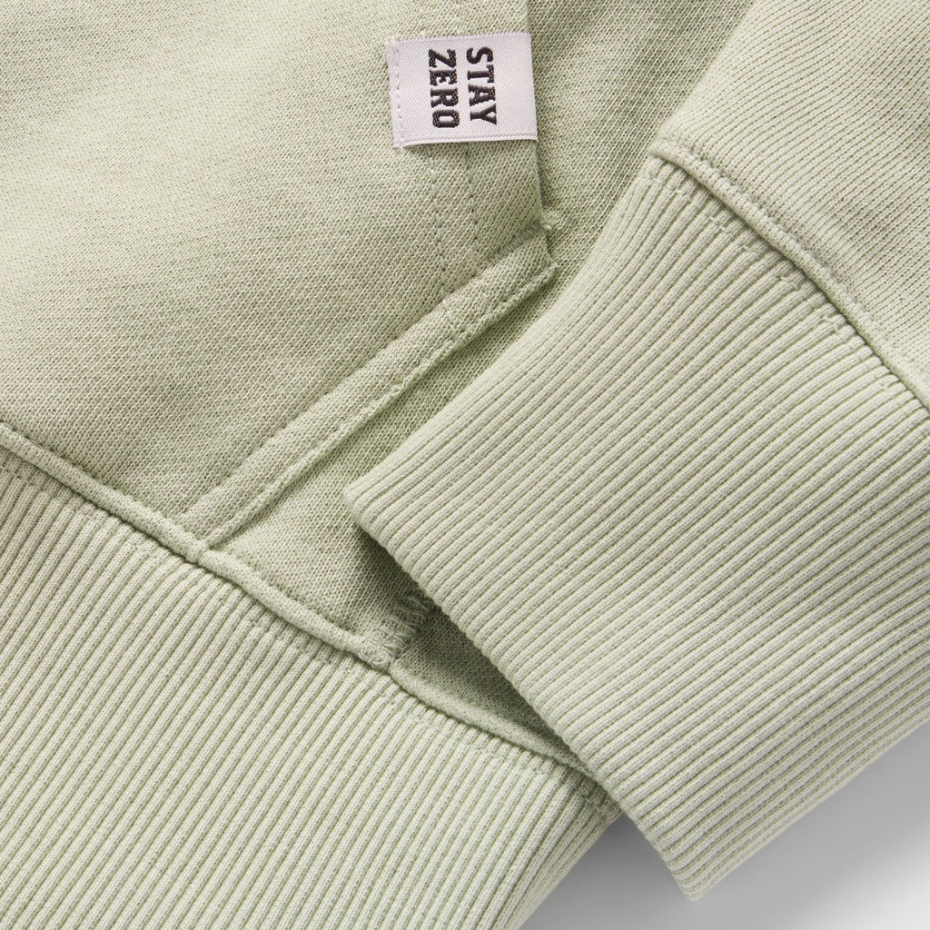 Close-up detail of the cuff and hem stitching in a soft sage green fabric on a Smuggler French Terry Crew, featuring a small woven tag with "STAY ZERO" text.