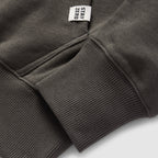 Close-up of a dark gray Smuggler French Terry Crew sleeve showing ribbed cuff detail and a small fabric tag with the text "STAY ZERO" attached near the seam.
