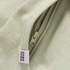 Close-up of a light sage green Smuggler French Terry Hoodie showing the textured fabric, zipper detail, and a "STAY ZERO" fabric tag.