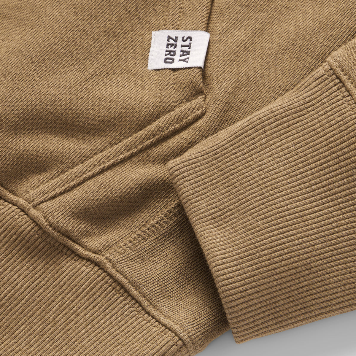 Close-up of the cuff and pocket stitching on a brown Smuggler French Terry Hoodie, featuring a small white tag with the text "STAY ZERO" for a clean, casual look.