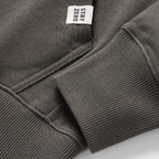Close-up detail of a dark gray Smuggler French Terry Hoodie showing the ribbed cuff, pocket stitching, and a small white fabric tag with "STAY ZERO" text.