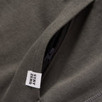 Close-up of an olive green Smuggler French Terry Hoodie featuring a black zipper pocket and a white fabric tag with the text "STAY ZERO" sewn into the seam.