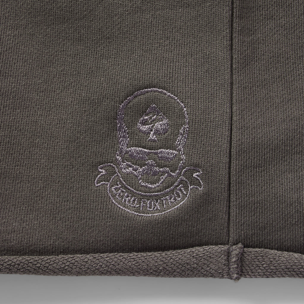 Close-up of embroidered logo detailing on dark fabric of Smuggler French Terry Jog Shorts - 6" Inseam, showcasing texture and stitching quality.