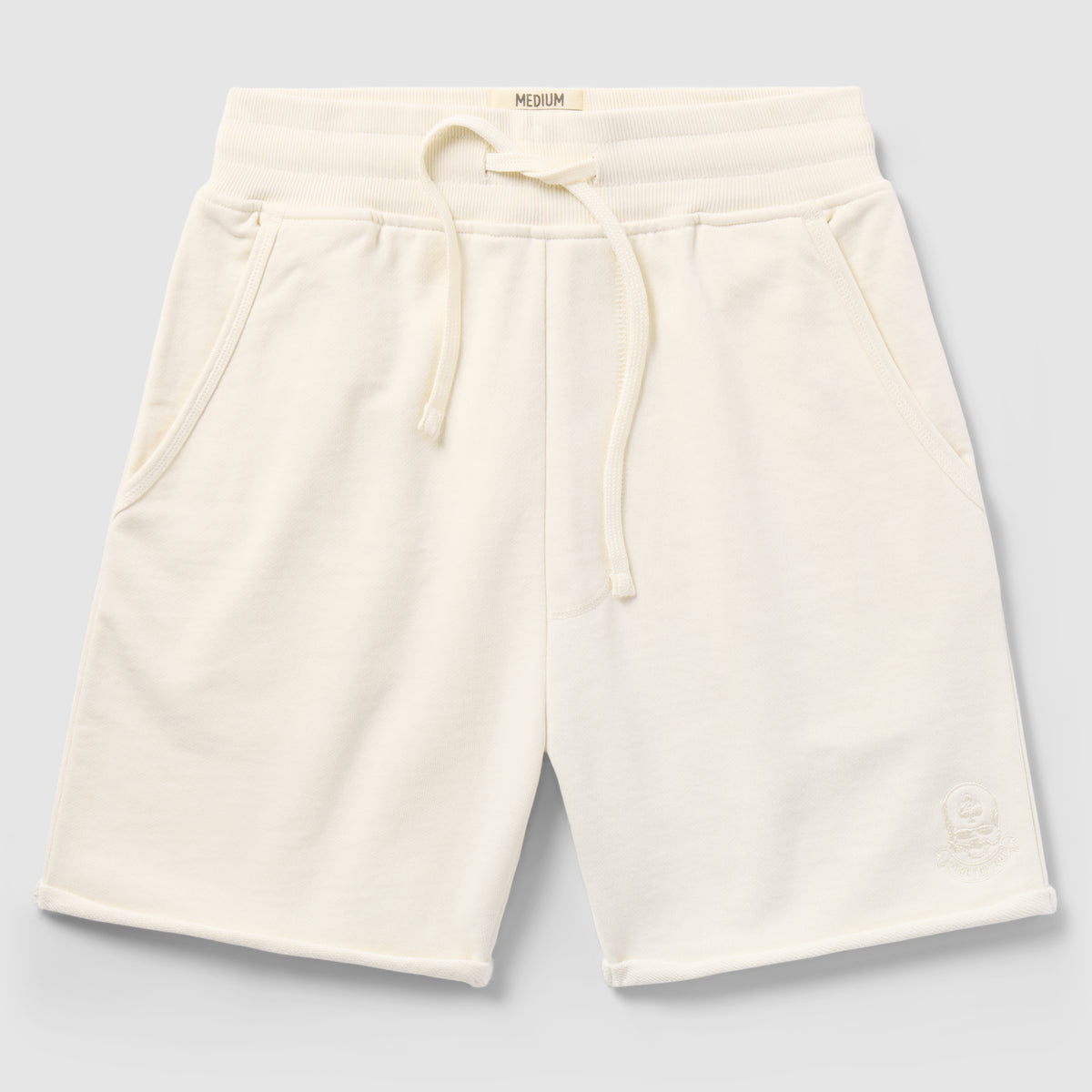 Cream-colored casual shorts with drawstring waistband and side pockets, featuring a subtle embroidered logo on the leg, Smuggler French Terry Jog Shorts - 6" Inseam.