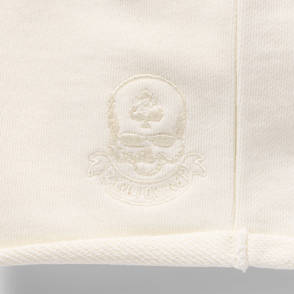 Close-up view of the embroidered logo detail on the light-colored fabric of the Smuggler French Terry Jog Shorts - 6" Inseam.