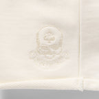 Close-up view of the embroidered logo detail on the light-colored fabric of the Smuggler French Terry Jog Shorts - 6" Inseam.