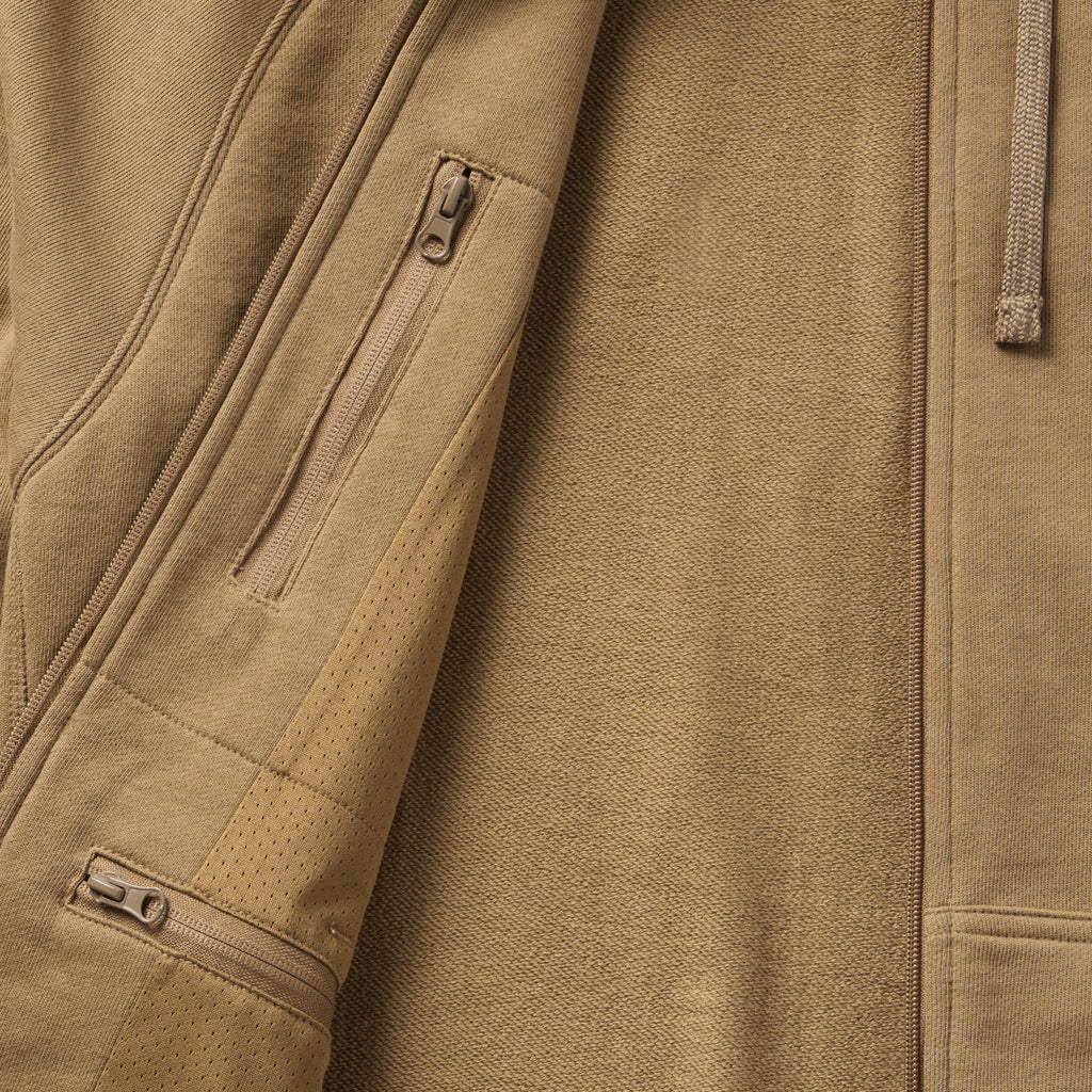 Close-up of tan fabric texture and zippered pockets detail on the Smuggler French Terry Zip Hoodie, highlighting its premium material and functional design features.