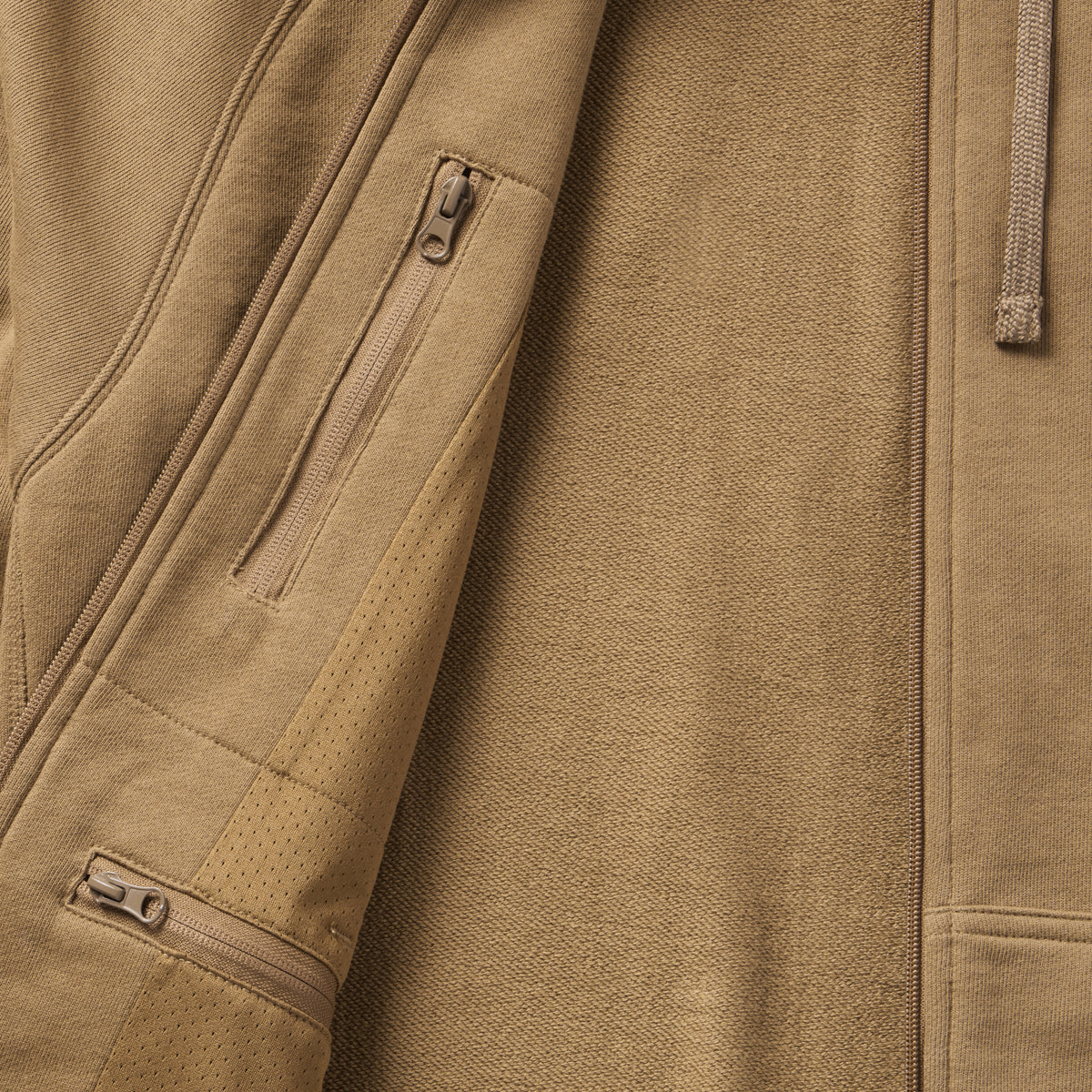 Close-up of tan fabric texture and zippered pockets detail on the Smuggler French Terry Zip Hoodie, highlighting its premium material and functional design features.