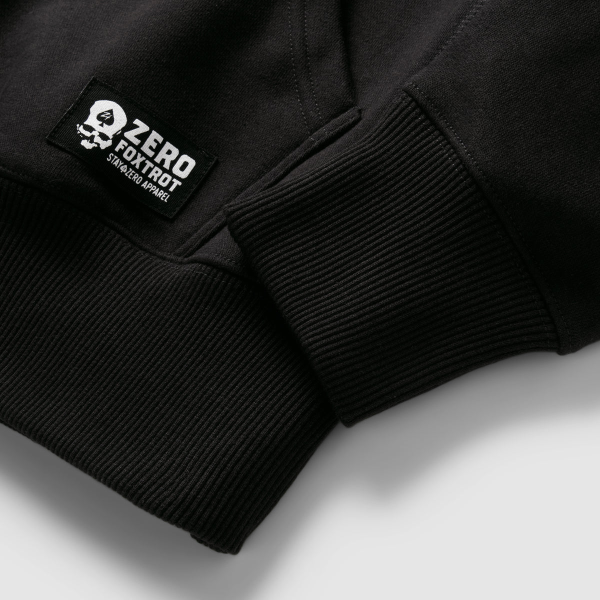 Smuggler Fleece Hoodie close-up showing black ribbed cuffs and a stitched logo label on soft fleece fabric