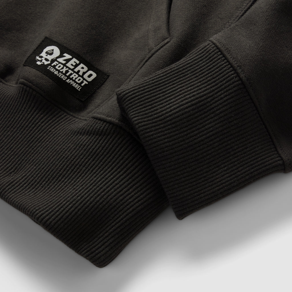Smuggler Fleece Hoodie close-up showing black ribbed cuffs, soft fleece fabric, and a sewn sleeve label on the dark outerwear garment