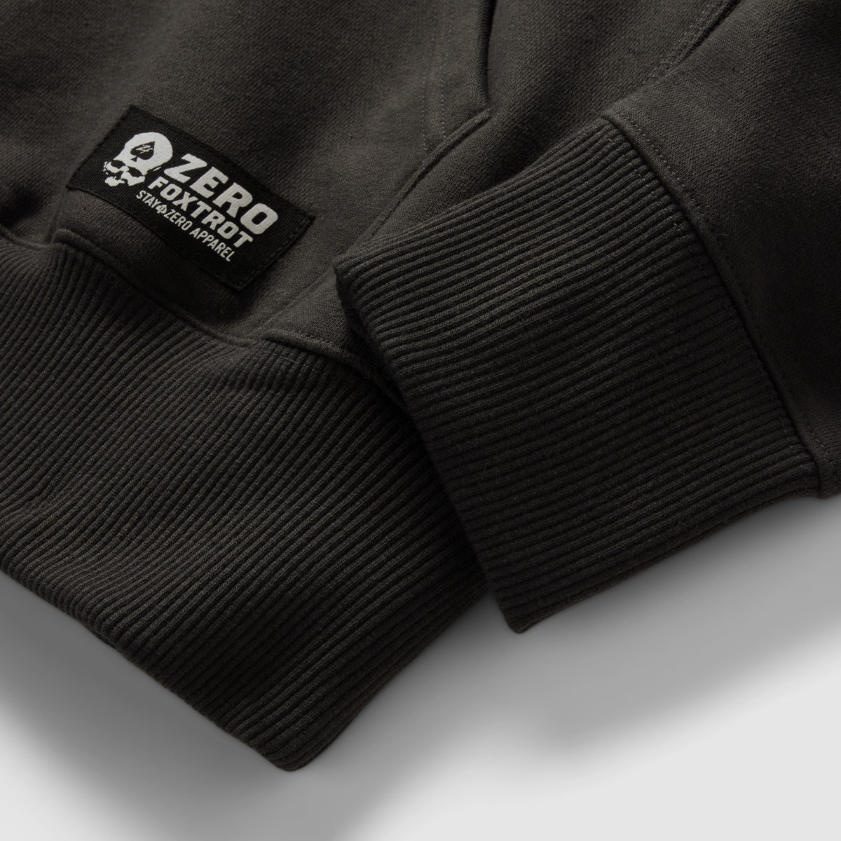 Smuggler Fleece Hoodie close-up showing black ribbed cuffs, soft fleece fabric, and a sewn sleeve label on the dark outerwear garment