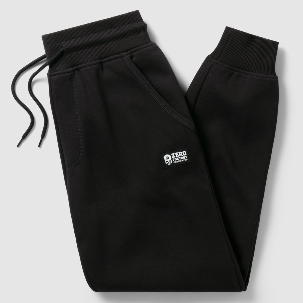 Smuggler Fleece Jogger in black with an elastic drawstring waistband, angled zip pocket, ribbed cuffs, and a small white logo on the thigh