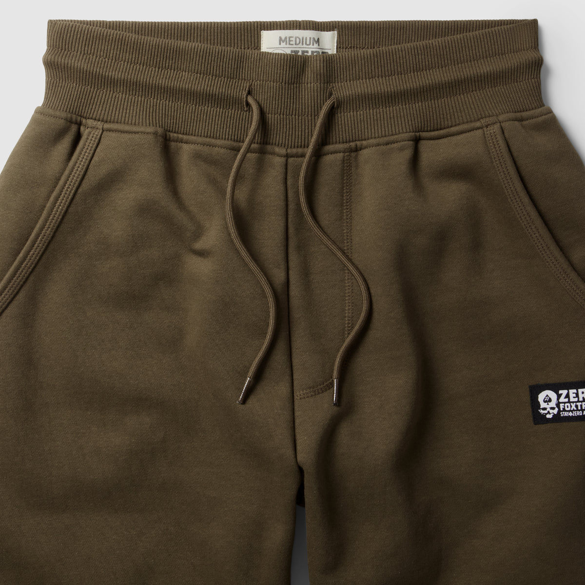 Smuggler Fleece Jogger in olive brown with a ribbed waistband, adjustable drawstring, front pockets, and a small logo patch on the leg