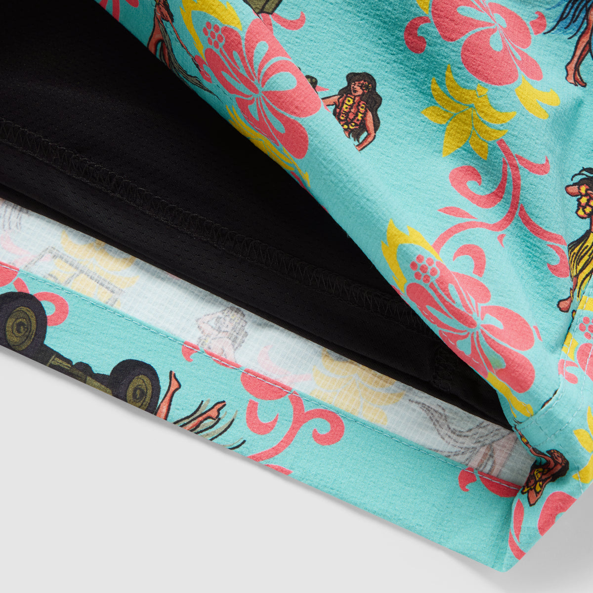 Close-up of a bright blue fabric with colorful pink and yellow floral prints and small hula dancer illustrations on Hula Tank Swim Trunks, showing detailed stitching and inner lining.
