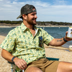 Surf Shirts (Last Chance) green patterned button up shirt worn by a smiling man sitting by the beach and holding a drink