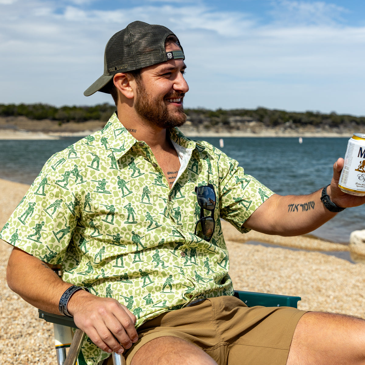 Surf Shirts (Last Chance) green patterned button up shirt worn by a smiling man sitting by the beach and holding a drink