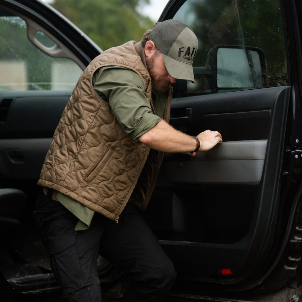 Woobie Vest (Last Chance) in brown, shown on a man wearing it over a green shirt as he steps out of a vehicle with the door open