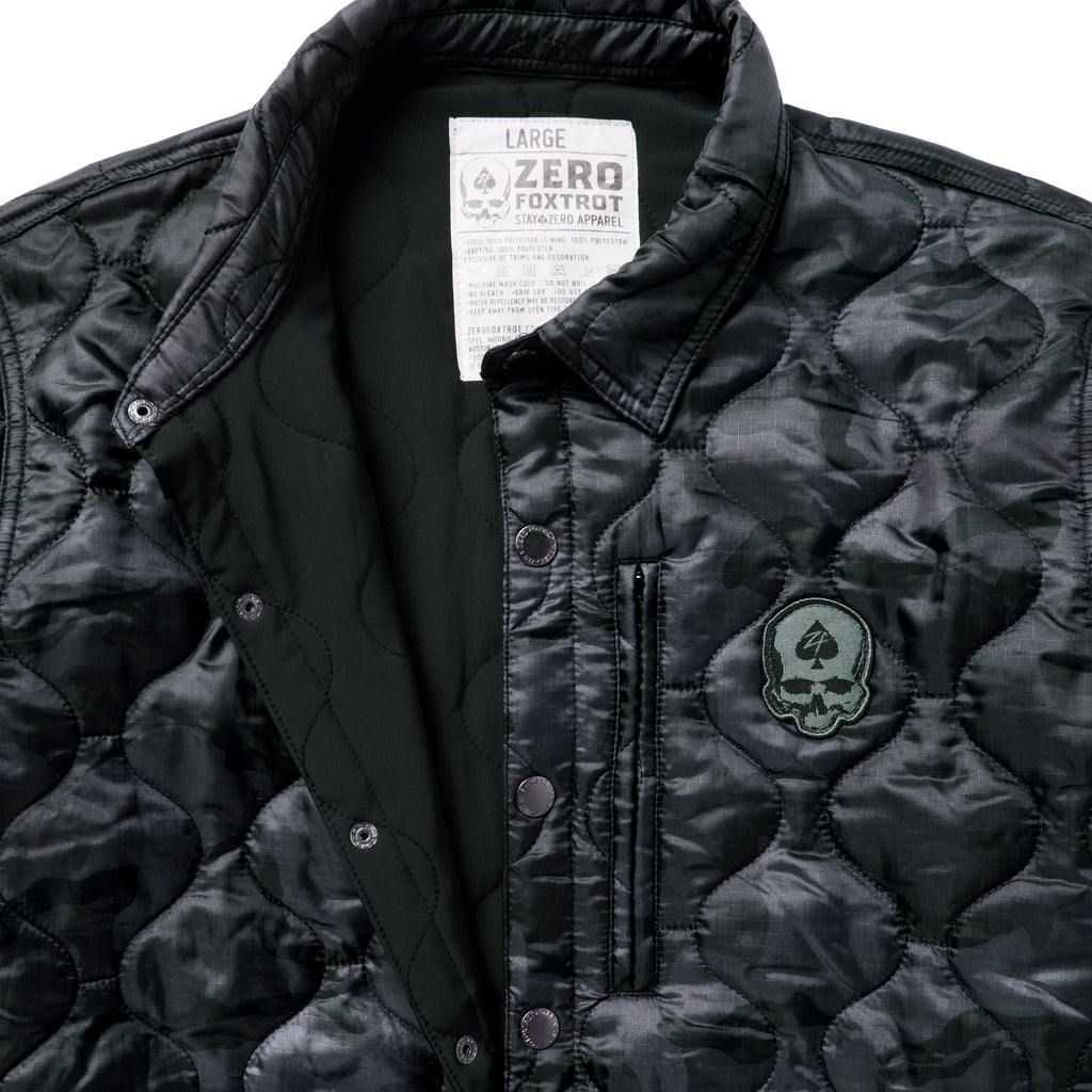 Woobie Shacket featuring black quilted camouflage fabric a snap front collar zippered chest pocket and skull patch detail close up view