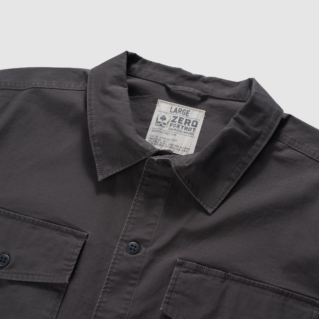 Close-up of a charcoal CPO Shirt showing the collar, button-front closure, and two chest pockets with buttons on a soft textured fabric.